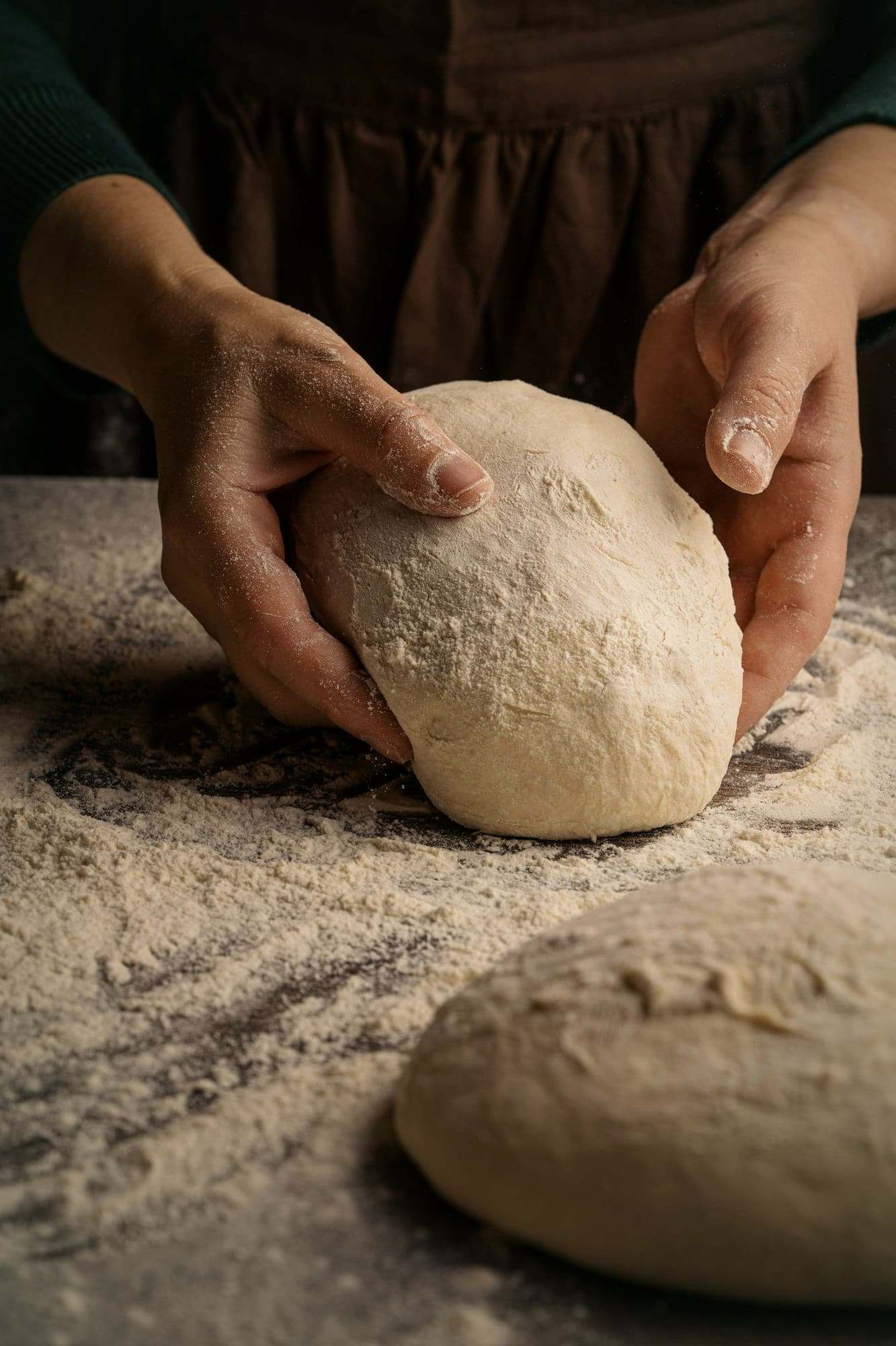 Two hands shaping a ball of dough on a floured table.