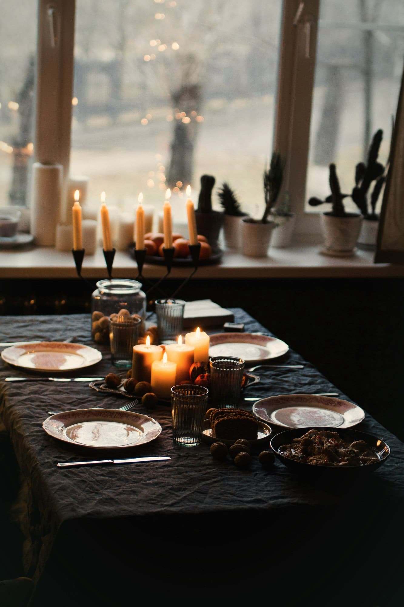 A table laid with plates and lit candles beside a window.