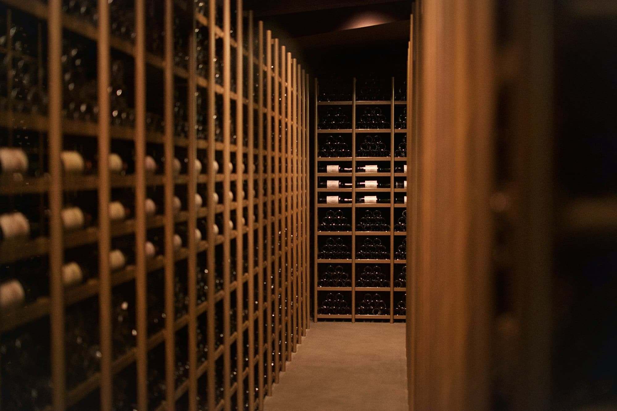 Floor-to-ceiling wooden racks of wine bottles along a cellar corridor.