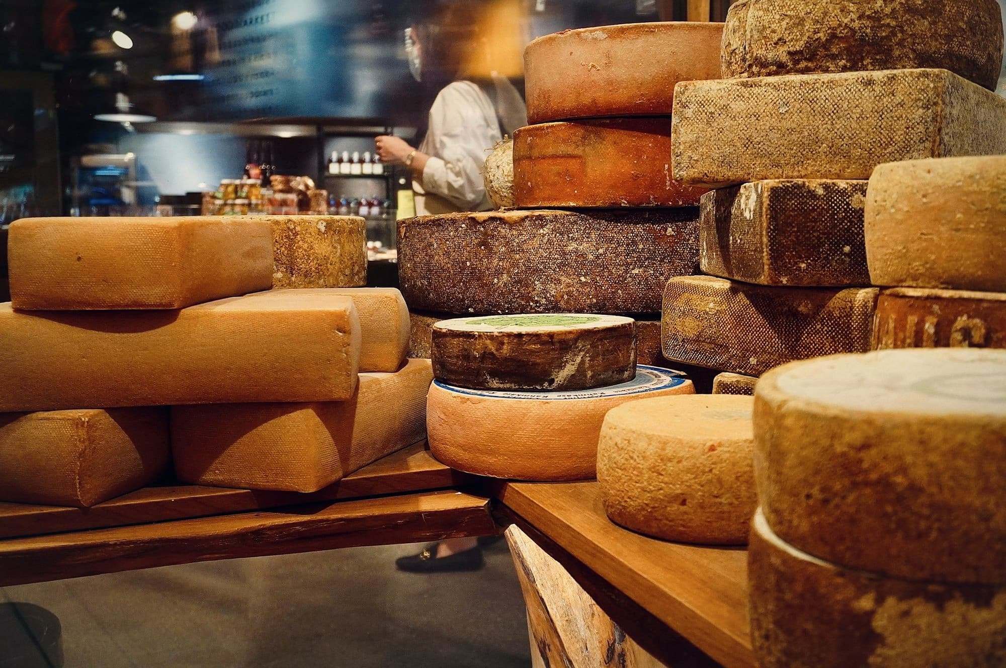 Wheels of aged cheese stacked on wooden shelves.