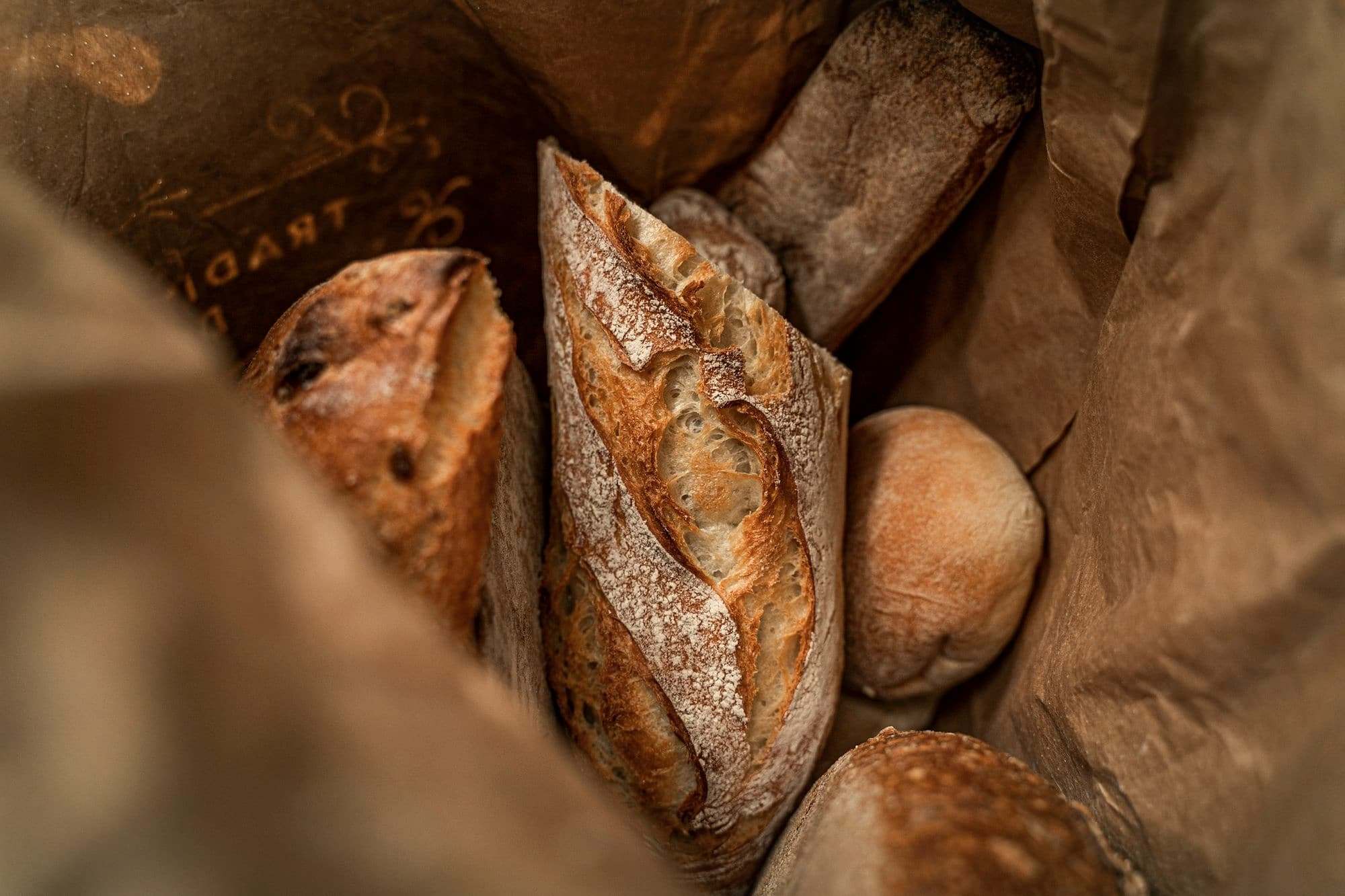 Crusty loaves and baguettes in a brown paper bag.