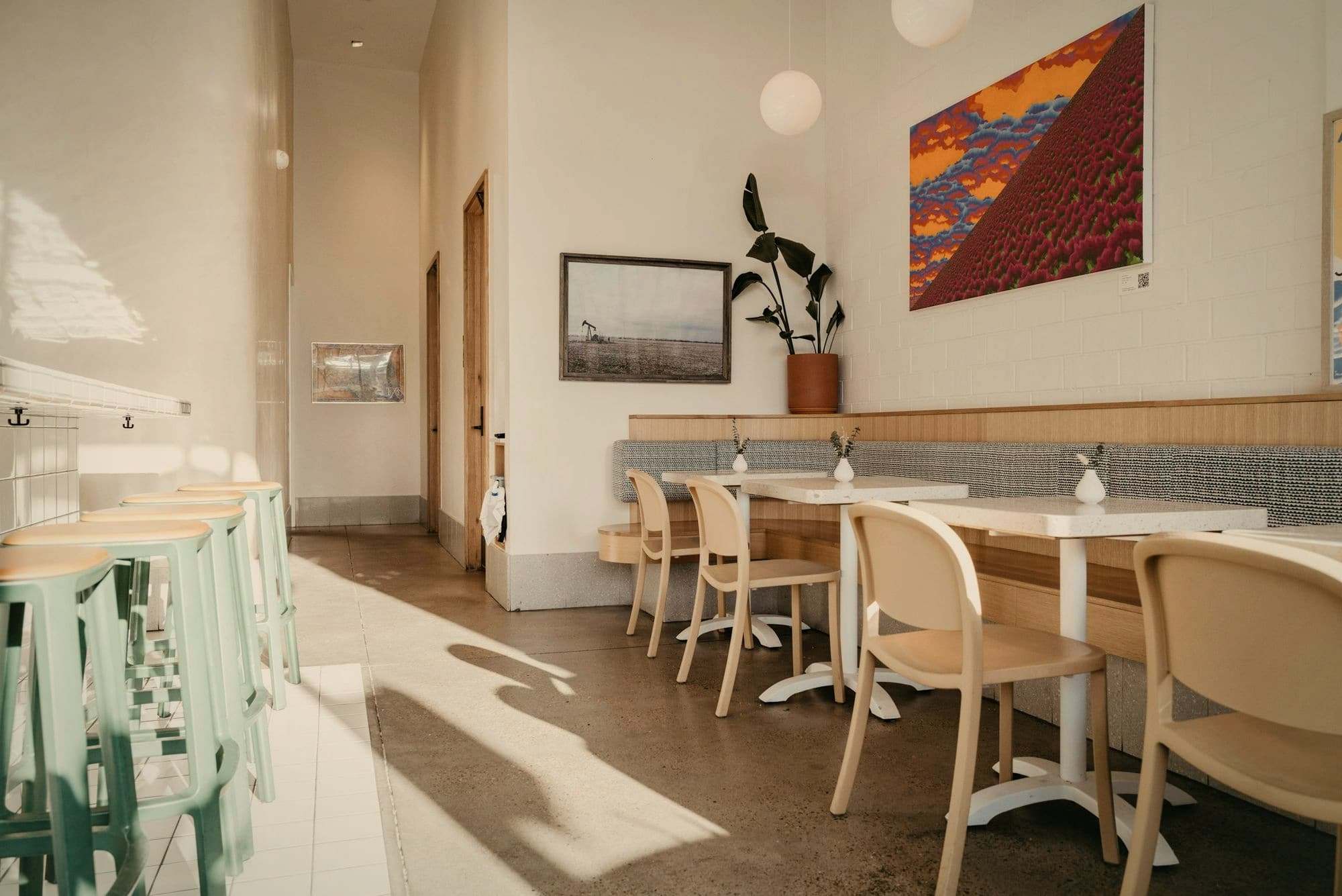 Sunlit café tables and wooden chairs along a pale wall.