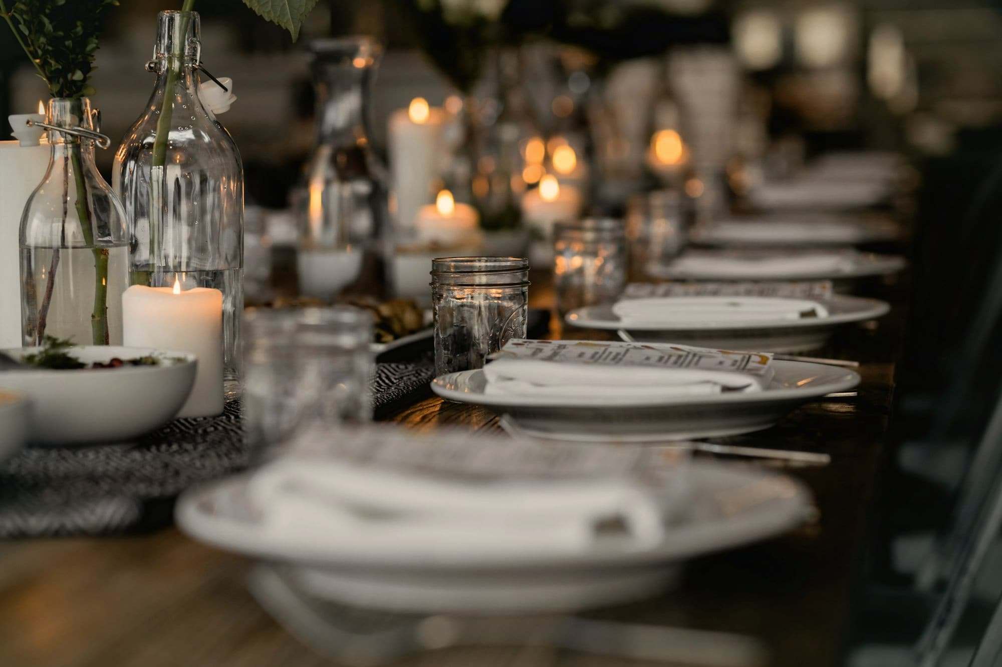 A long wooden table set with plates, glass bottles and candles.