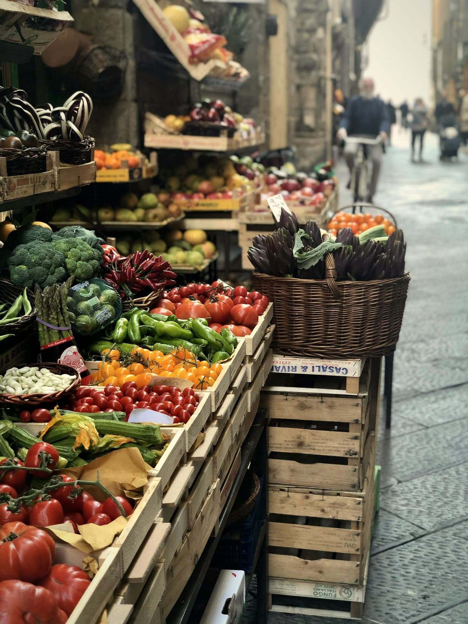 Crates of vegetables and a wicker basket of artichokes at a market stall.