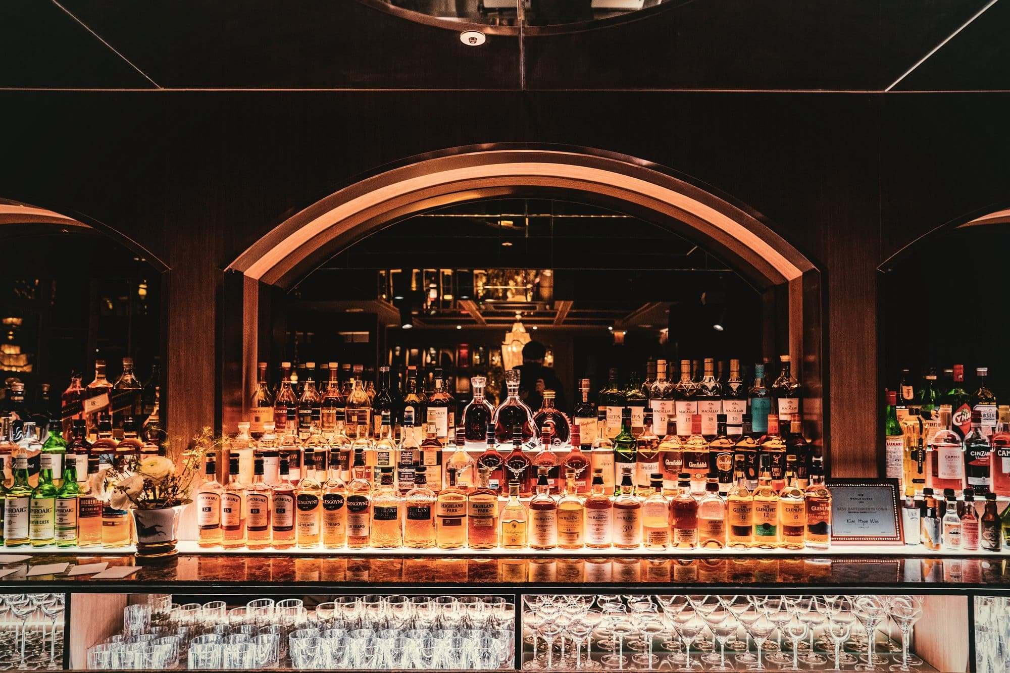 The back bar at Salt Room under a copper arch, with rows of bottles glowing.