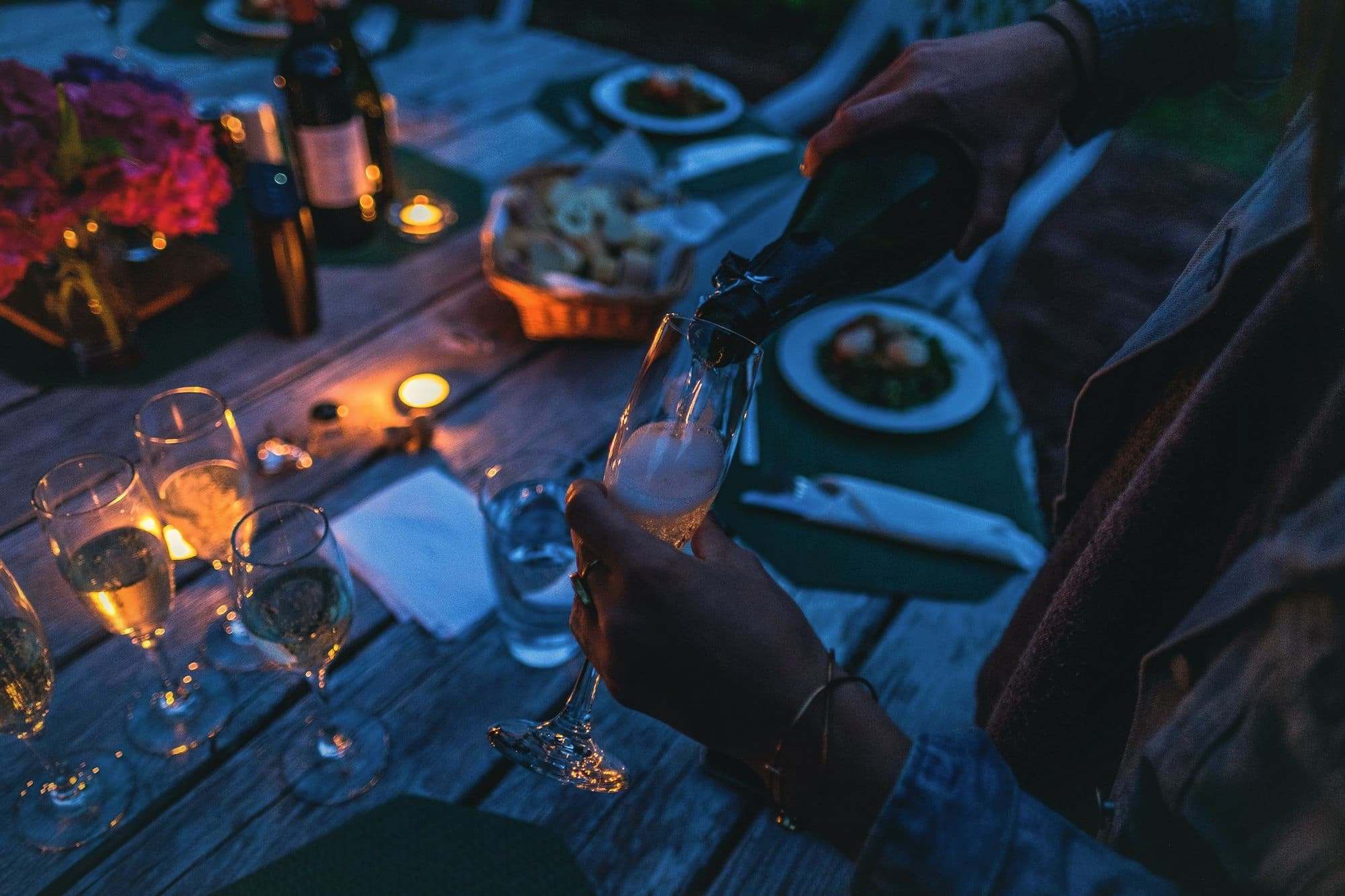 Sparkling wine being poured into a glass at an evening table.